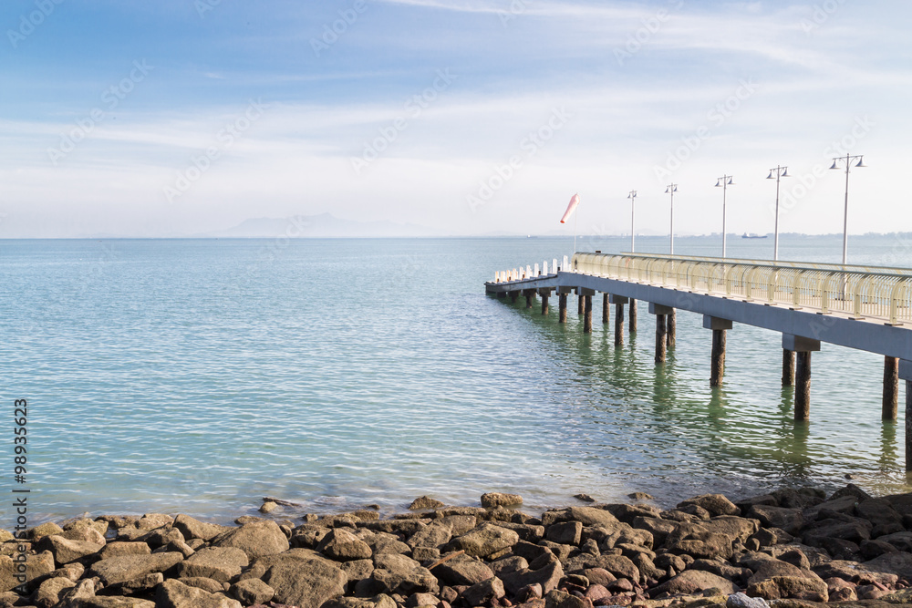 Jetty on the coast reaches out to calm blue sea Jetty on the coast reaches out to calm blue sea