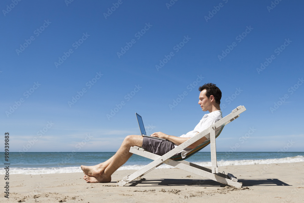 Happy young freelancer working online with laptop on a beach