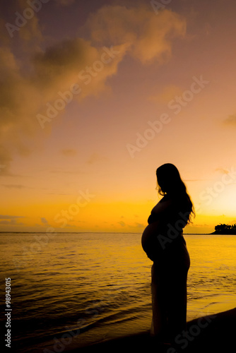 Silhouette of pregnant woman on the beach at sunset during the g