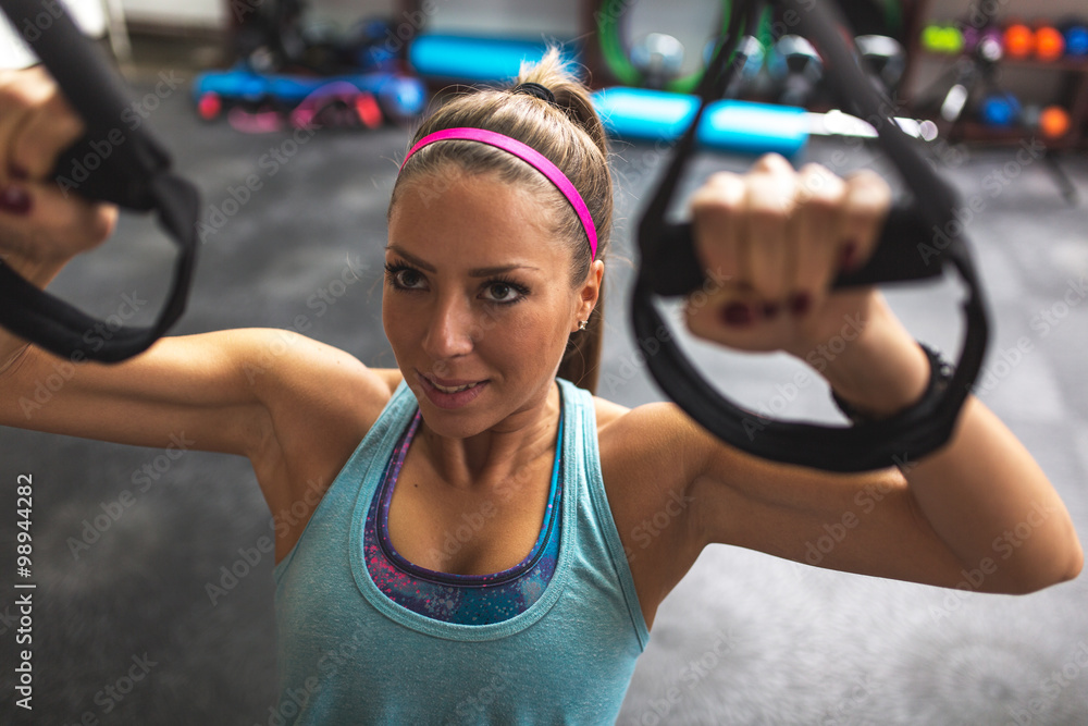 Obraz premium Young female at the gym working on her abs on trx