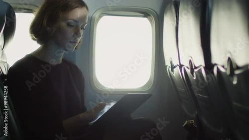 Young woman is using a tablet inside an airplane next to a window. Shot on RED Cinema Camera.