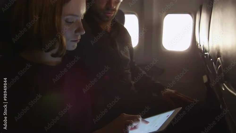 Couple are sitting together on a plane and using tablet. Shot on RED Cinema Camera. Couple are sitting together on a plane and using tablet. Shot on RED Cinema Camera.
