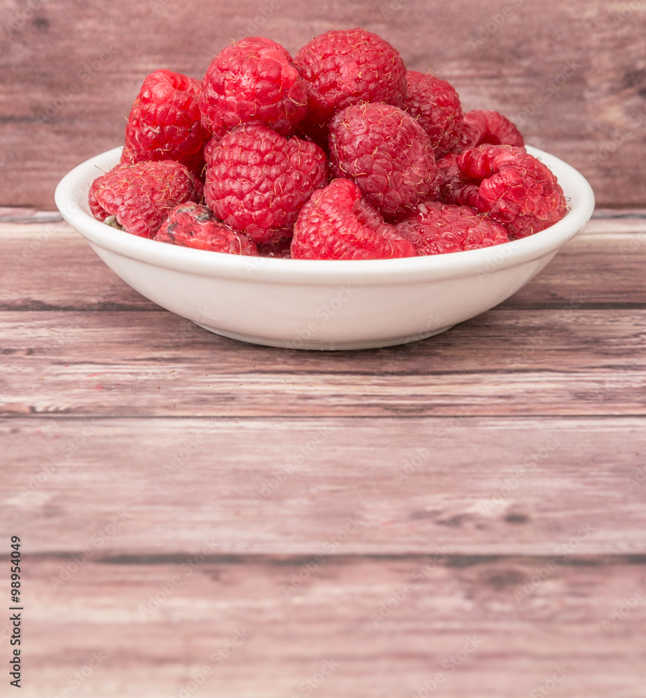 Raspberry fruit in white bowl over wooden background Raspberry fruit in white bowl over wooden background