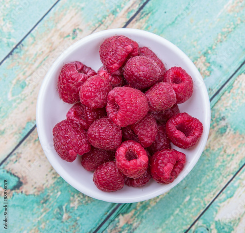 Raspberry fruit in white bowl over wooden background