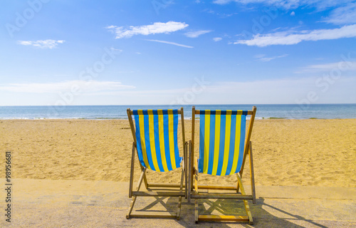 Two blue and yellow deckchairs facing the sea across golden sand