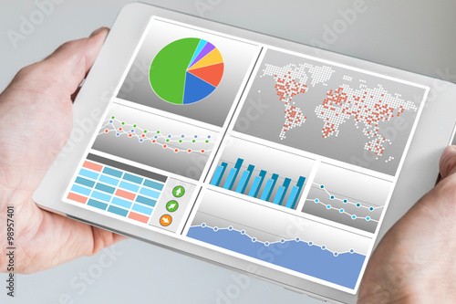 Hand holding modern tablet or mobile device with analytics dashboard for sales, marketing, accounting, controlling department to check revenue, sales and business KPIs