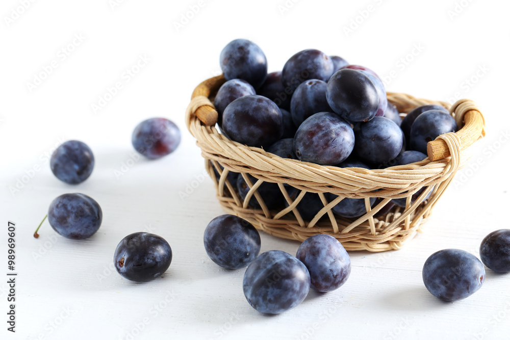 Fresh plums in basket on the white wooden background Fresh plums in basket on the white wooden background