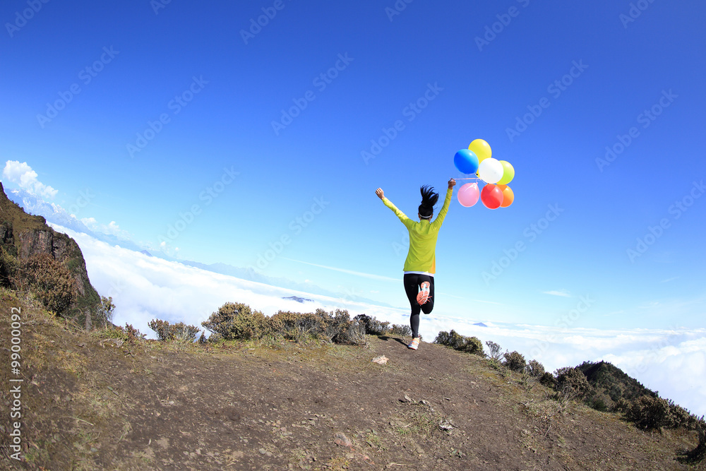 Obraz premium young cheering woman running with colorful balloons on mountain peak