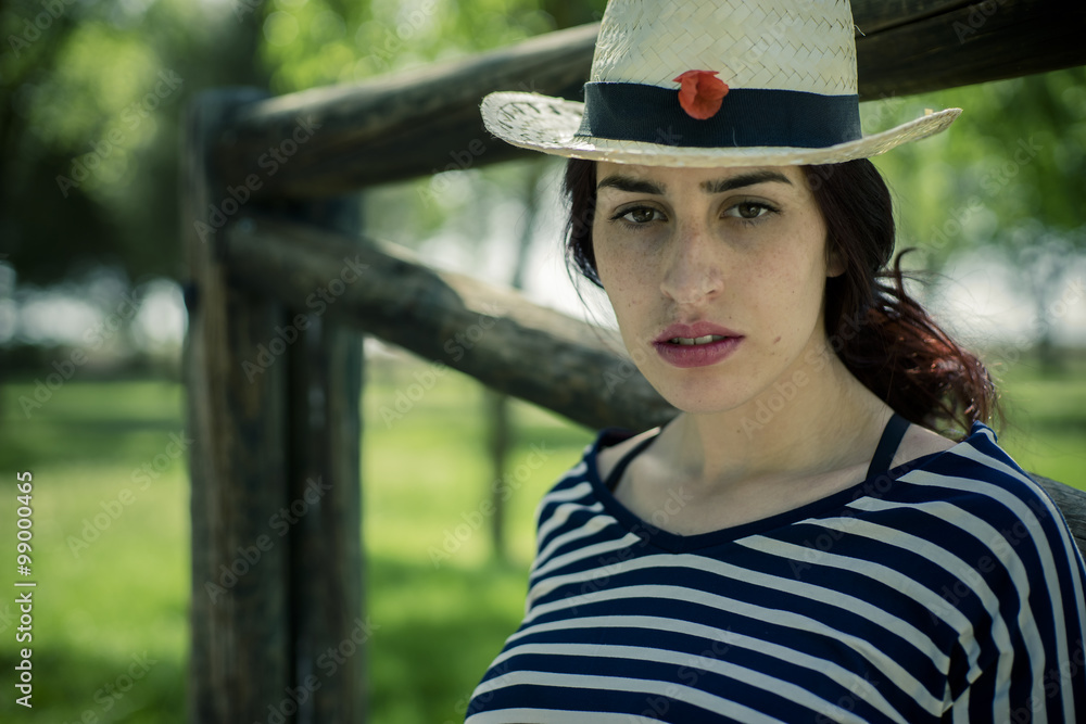 Alone girl with straw hat sitting on a wooden bridge in a park i Alone girl with straw hat sitting on a wooden bridge in a park i