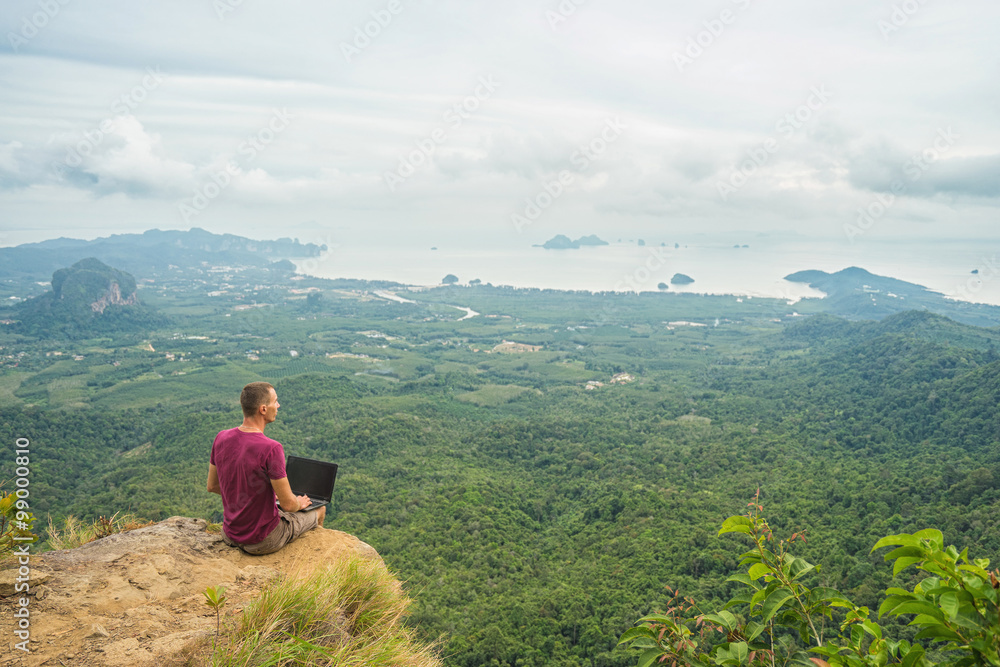 Man working with laptop sitting on the rocky mountain on beautiful scenic clif background.  Thailand. Krabi .