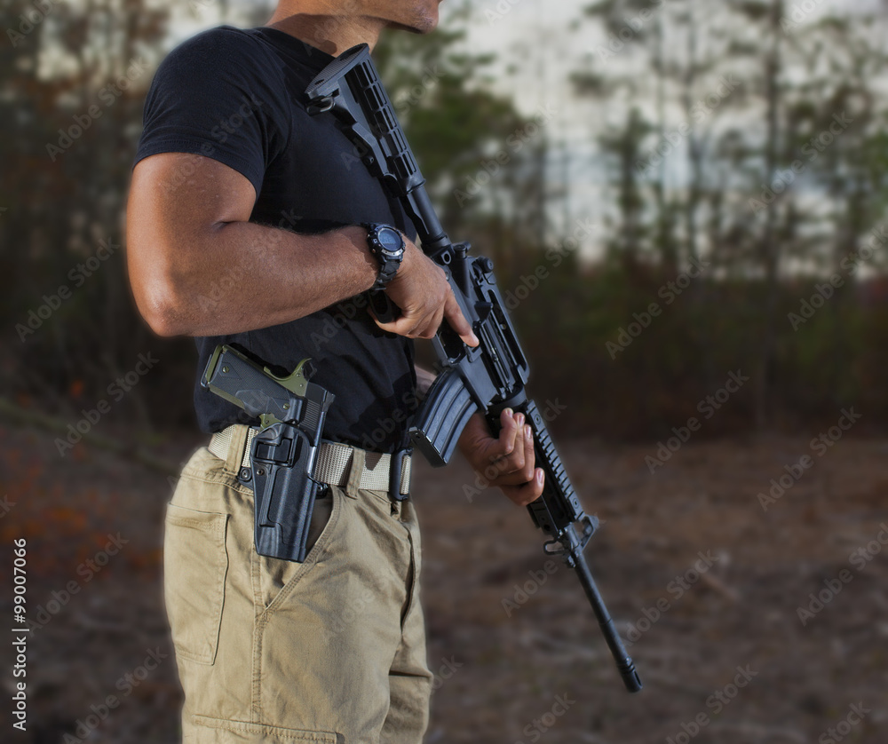Gun owner with an assault rifle outdoors and a semi-auto pistol strapped to his side. Gun owner with an assault rifle outdoors and a semi-auto pistol strapped to his side.