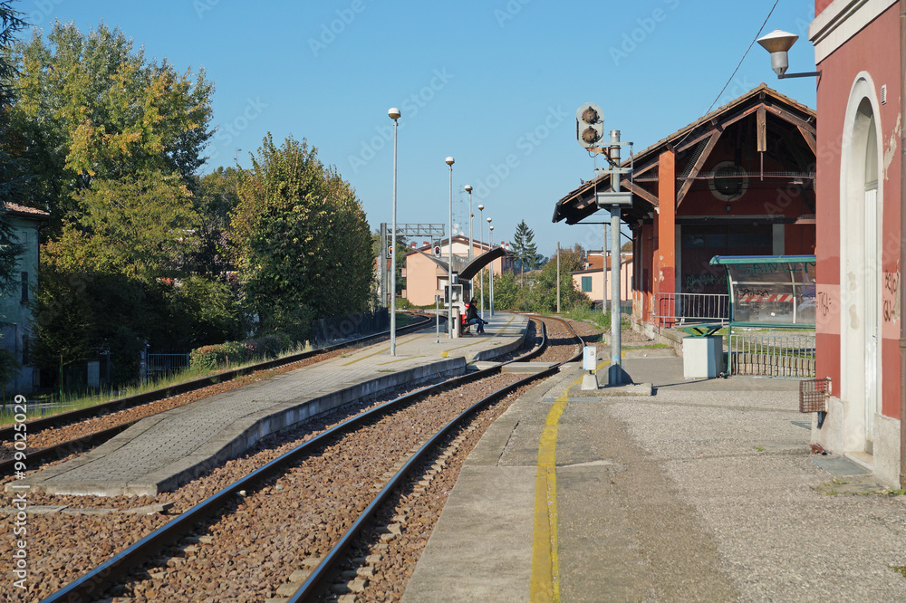small train station in the rural outskirts, with people waiting for the local train