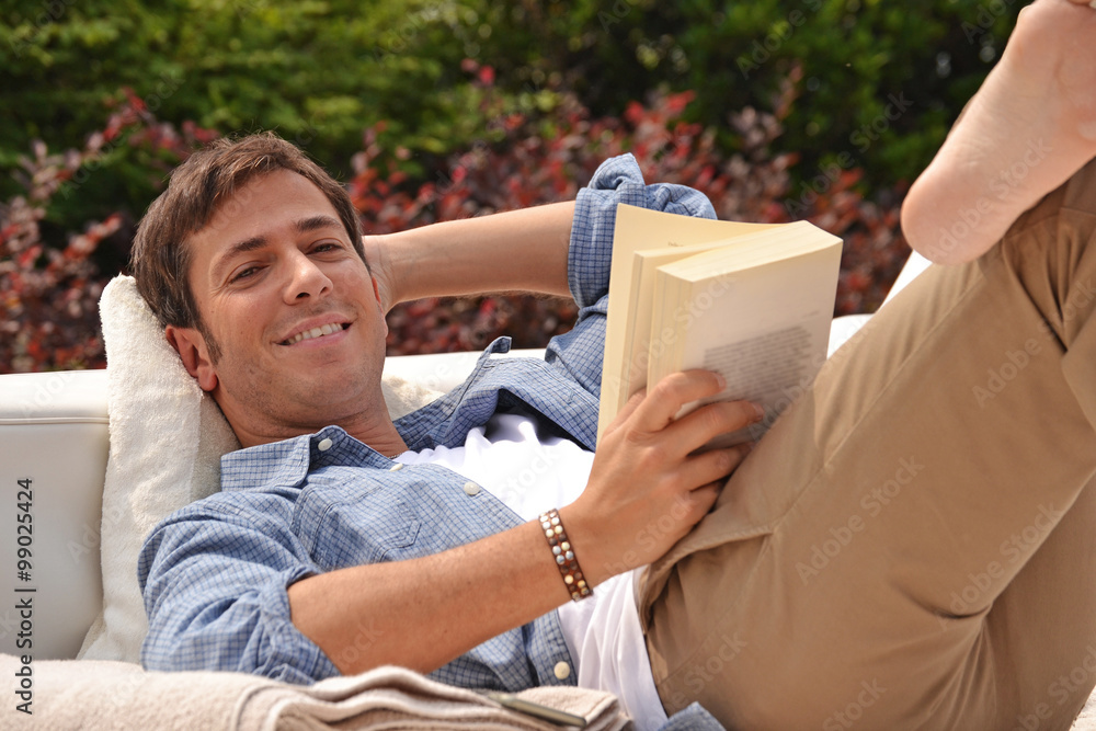 Hombre relajado recostado leyendo un libro en la piscina de su casa. - obrazy, fototapety, plakaty 