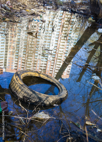 Garbage, old tire and reflection of the high-rise in the water
