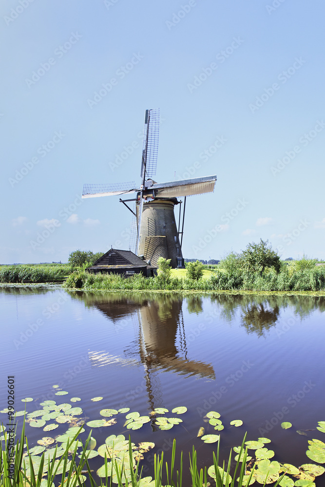 Ancient wind mill reflected in a blue canal on a summer day, Kinderdijk, The Netherlands