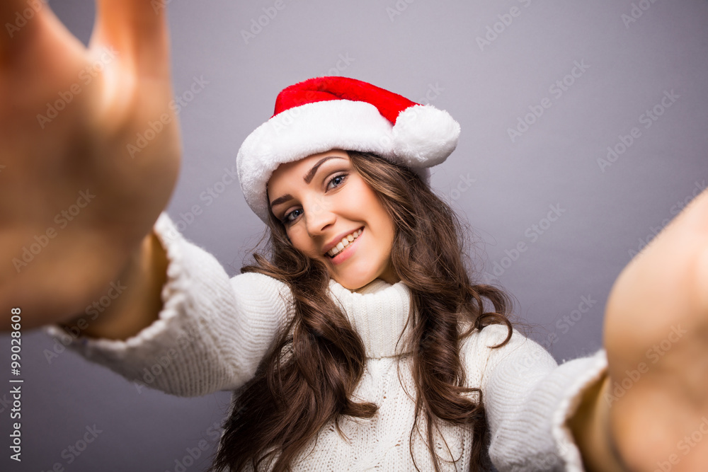 Christmas portrait of beautiful girl. Girl wearing santa claus hat. Girl smiling and making selfie on mobile phone Christmas portrait of beautiful girl. Girl wearing santa claus hat. Girl smiling and making selfie on mobile phone