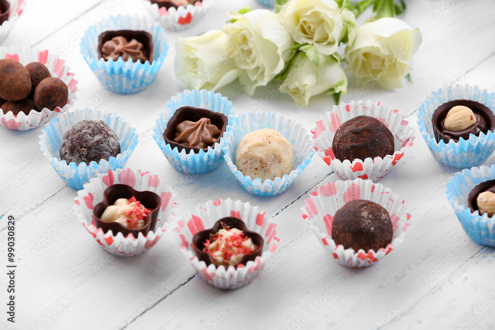 Set of chocolate candies with flowers on a light wooden background Set of chocolate candies with flowers on a light wooden background