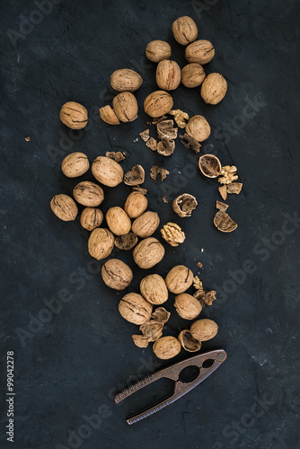 Walnuts with nutcracker over  black slate stone background