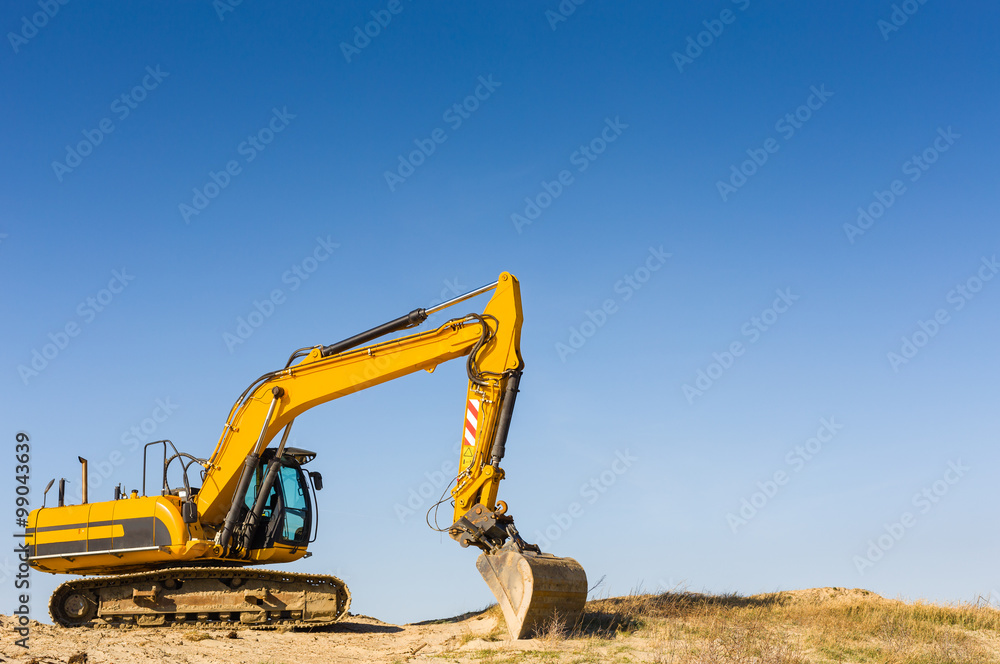 Yellow excavator on the beach under a blue sky