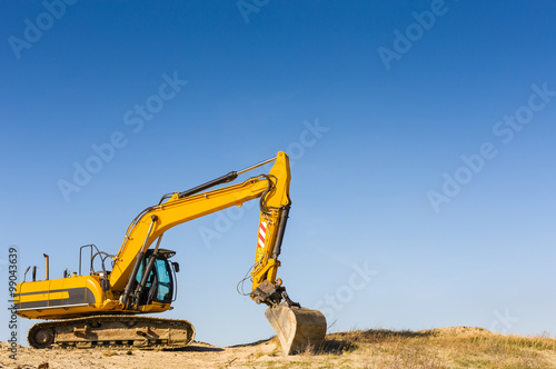 Yellow excavator on the beach under a blue sky