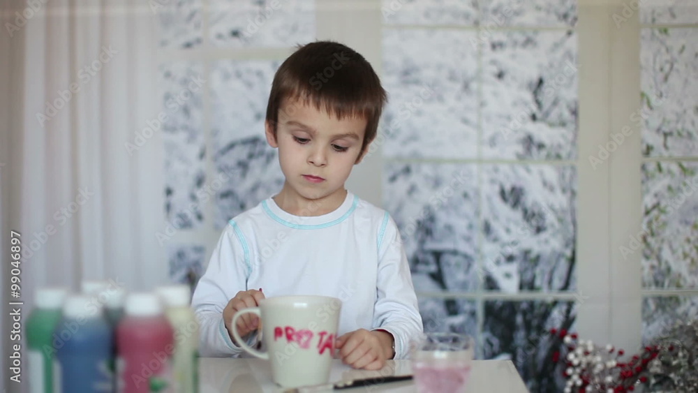 Cute little preschool boy, drawing picture on mug for his fathers birthday at home, wintertime Cute little preschool boy, drawing picture on mug for his fathers birthday at home, wintertime