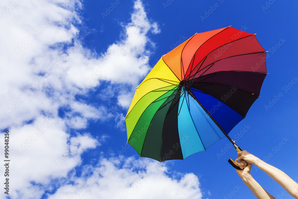 multicolored umbrella in hand on background sky