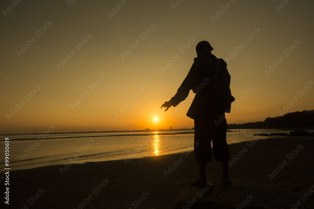 silhouette of man trying to catch the sun during sunset at the beach