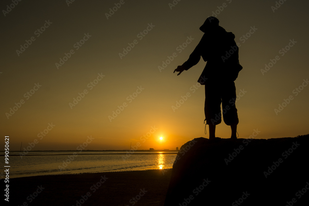 silhouette of man trying to catch the sun during sunset at the beach