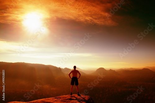 Red filter photo. Naked climber in black pants gesture of triumph. Tourist on peak of sandstone rock in national park Saxony Switzerland