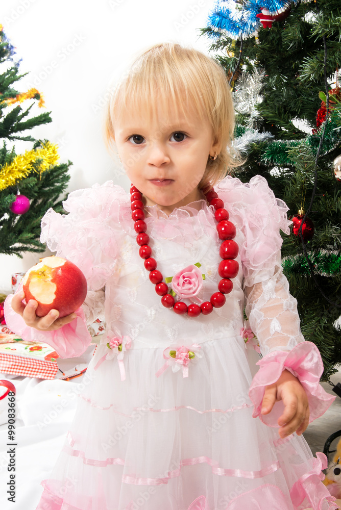 Little girl near the Christmas tree eats an apple