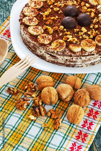 Chocolate cake with nuts and bananas on a plate and walnuts on a yellow napkin