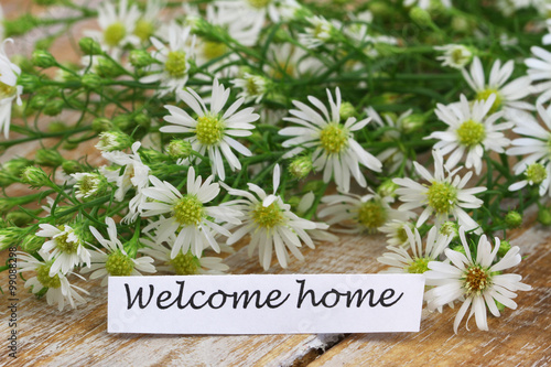 Welcome home card with chamomile flowers on rustic wooden surface
