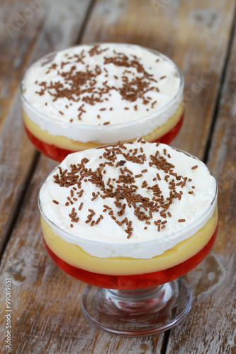 Two strawberry trifle desserts with fresh whipped cream and sprinkled with chocolate on rustic wooden surface
