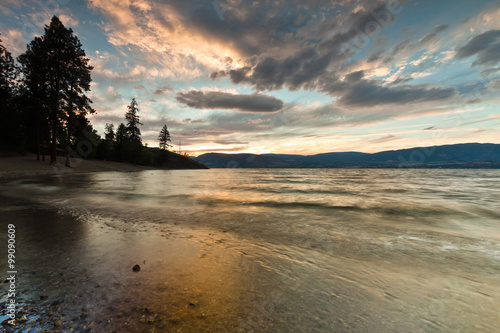 sunset on mountain lake from sandy beach shore