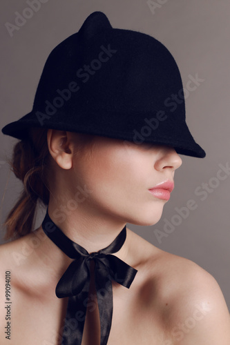 beautiful woman with dark hair wears elegant black hat and silk bow on neck