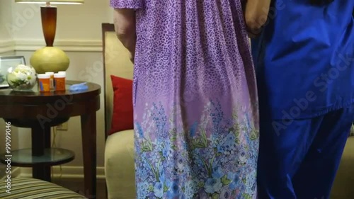 A Hispanic home health practical nurse assist her elderly patient into the living room for weekly health visit.