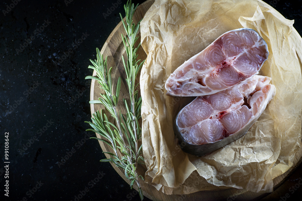 Obraz premium Fillet of raw fish and ingredients for cooking on a dark background in a rustic style. View from above