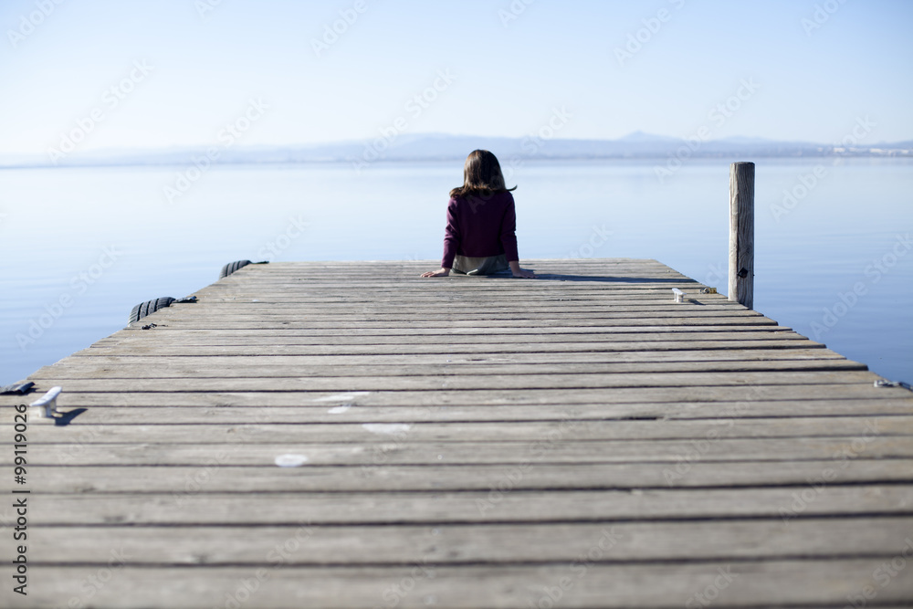 Naklejka premium Niña solitaria sentada en muelle de madera