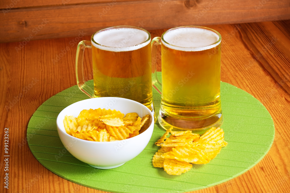 Beer mugs and potato chips on wooden table
