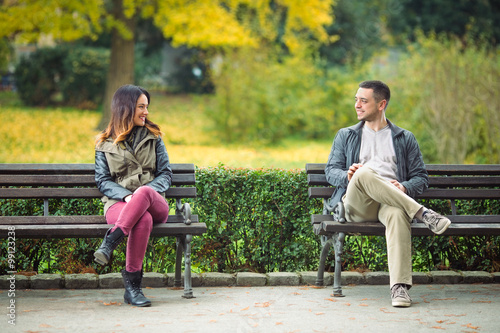 Two young people sitting on benches in a park and talking