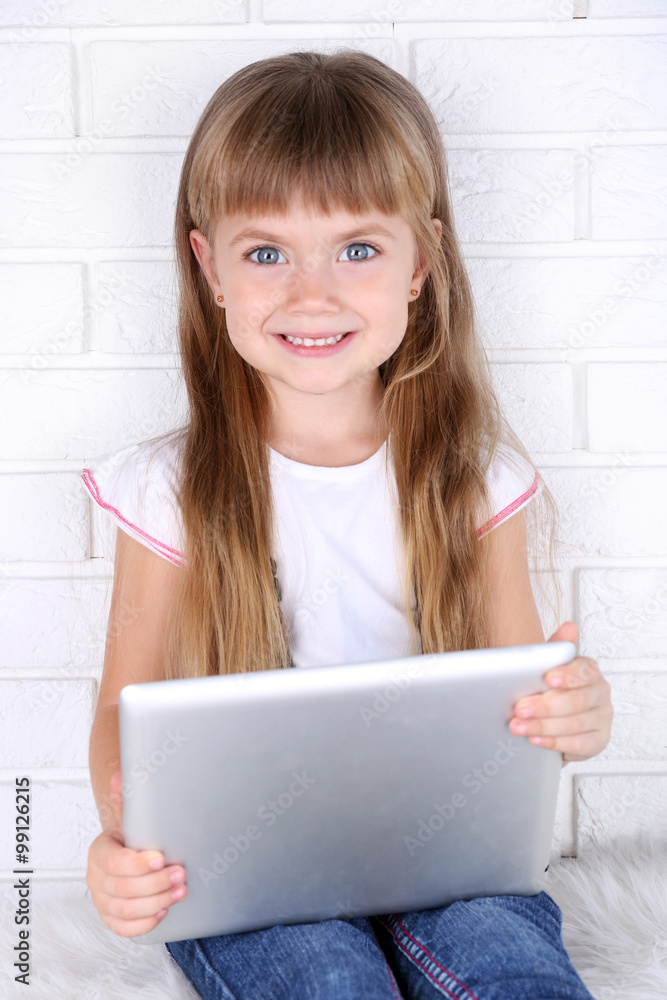 Little girl with tablet on brick wall background Little girl with tablet on brick wall background