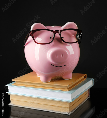 Piggy bank with glasses and books on a black background