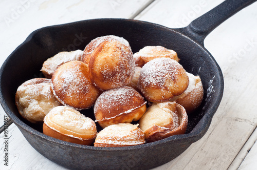 Danish style aebleskiver apple pancakes or pancake puffs served in a cast iron pan on white rustic boards.