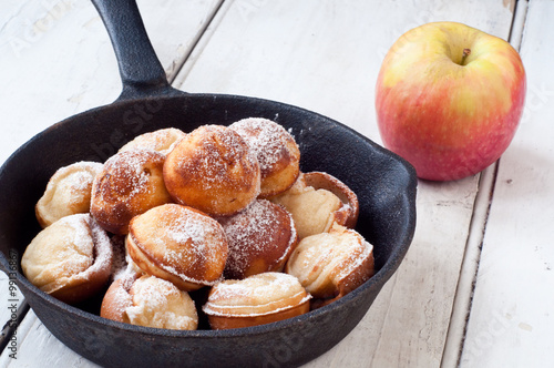 Danish style aebleskiver apple pancakes or pancake puffs served in a cast iron pan on white rustic boards.