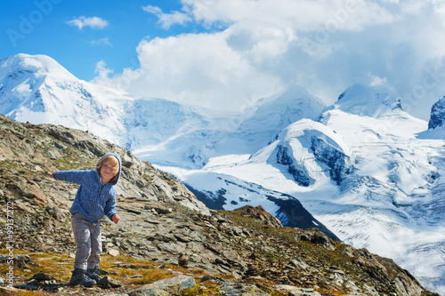 Cute kid boy resting in Alps, wearing warm knitted jacket and mountain boots