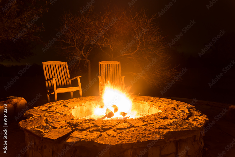 Fire pit aflame with two empty chairs and dark forest - obrazy, fototapety, plakaty 