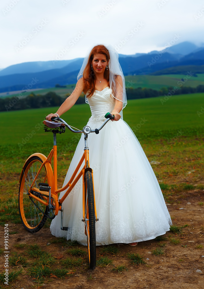 Fototapeta premium bride on orange bike in beautiful wedding dress with lace in landscape.