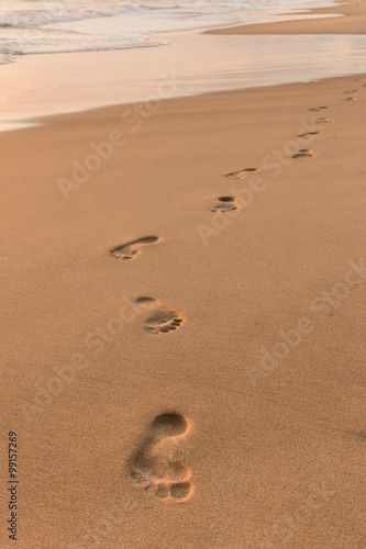 Картината върху платно footprints on sandy beach at sunrise