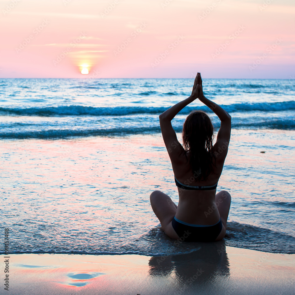 Silhouette woman yoga on the beach at sunset in South Asia.