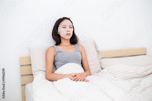 Woman using facial mask and lying on bed